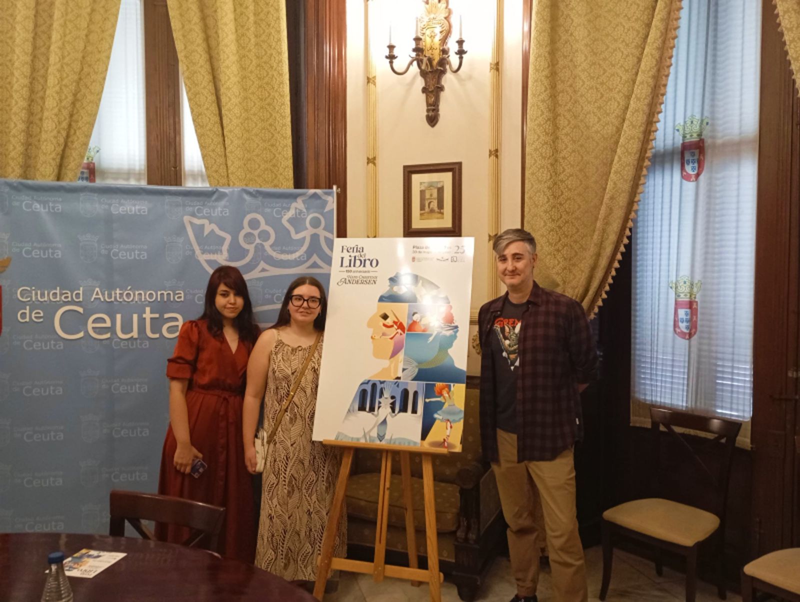 Las autoras del cartel, junto a  su obra y uno de los profesores / Coronado